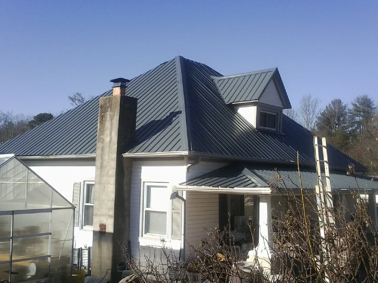 Dark blue standing seam metal roof on a white farmhouse with dormer — Slate & Tile Roof Repair by Roofing Brothers in Scribner