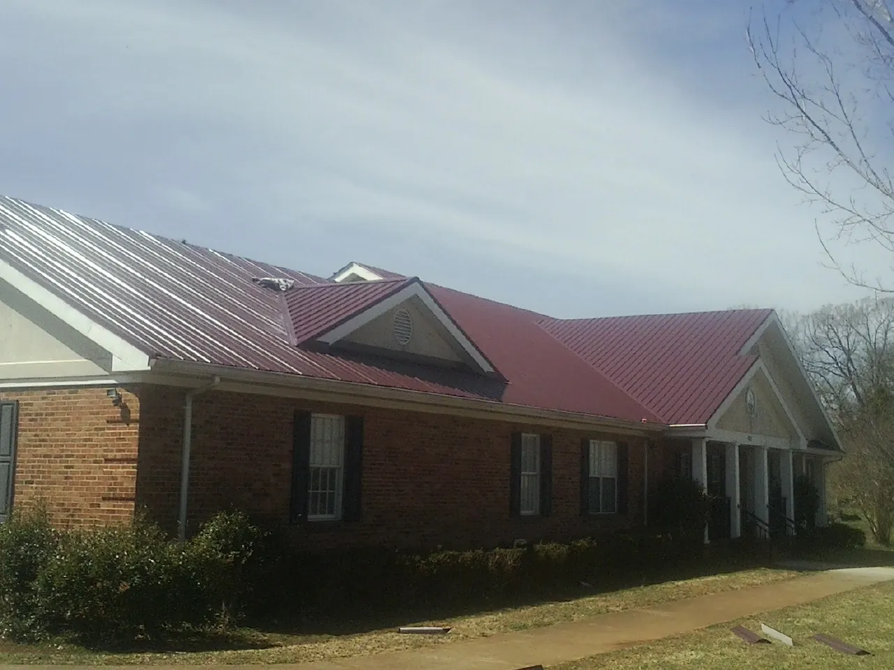 Red metal roof with gabled entries on a long brick building, from a Hail Damage Roof Repair job in Scribner