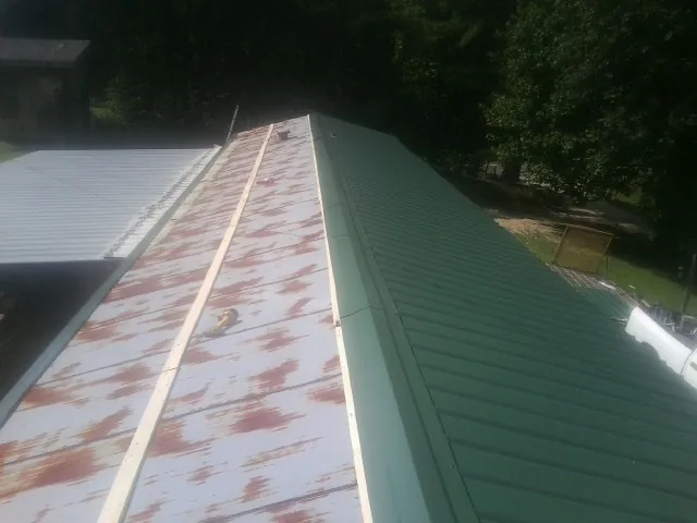 Old rusted panels beside newly installed green metal roofing — Wind Damage Roof Repair by Roofing Brothers in Scribner